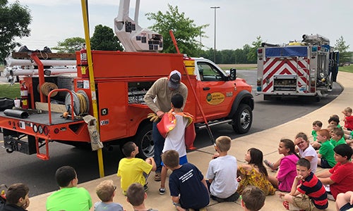 A lineman shows a group of children his equipment.