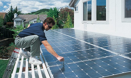A man installs solar panels on a roof.